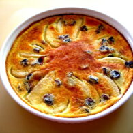Pear and dried cherry clafouti in a round baking dish, dusted with confectioner’s sugar and photographed just after baking.