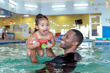 Adult holds smiling child up in pool