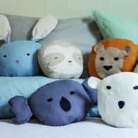 Handmade lion pillows and panda bath puppets from “Animal Friends to Sew,” arranged on a neatly made bed as inspiration for kid-friendly DIY sewing gifts.