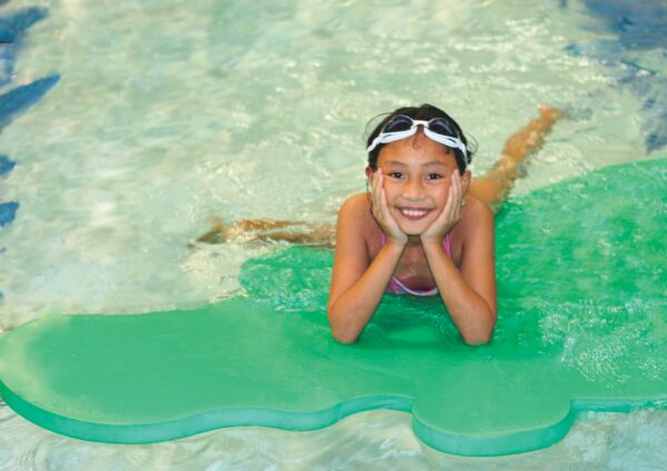 Girl lays on pool float with head propped on hands, smiling at camera