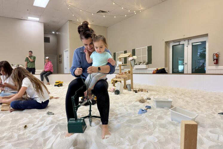 Mother and toddler sitting together on a toy digger inside SandGarden’s indoor sandbox in Issaquah
