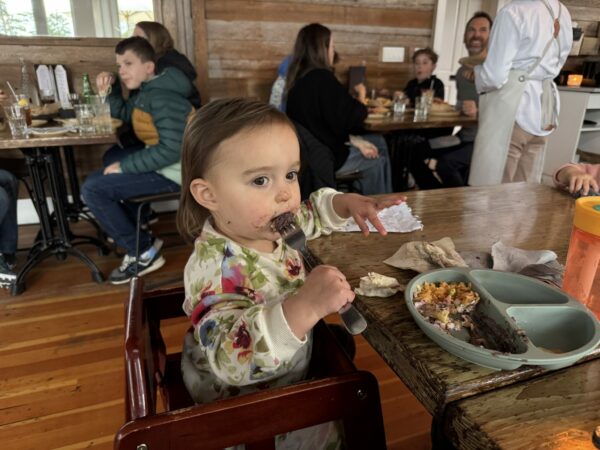 Toddler enjoying dinner at Koko’s Restaurant and Tequila Bar in Seabrook, Washington, smiling with food on her face while seated at the table.