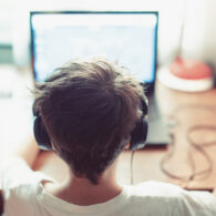 Back of child's head, with headphone on facing a computer screen at a desk