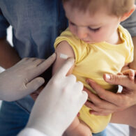 Pediatrician placing a bandage on a baby’s arm after vaccination.