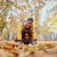 Happy kids having fun while playing in autumn leaves at the park and looking at camera.