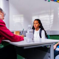 Teacher, parent and student sitting together at a classroom table reviewing student work during a parent-teacher conference.