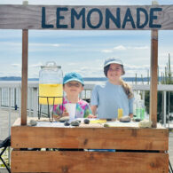 Etta, 10, and Hugo, 8, run a homemade lemonade stand, continuing a family tradition with the same wooden stand their dad used as a child.