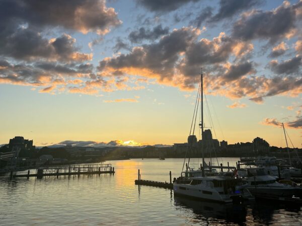 Sunset over water, against boats in harbor.