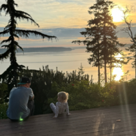 Parent and child sitting together at sunset with a backdrop of trees and water on Camano Island